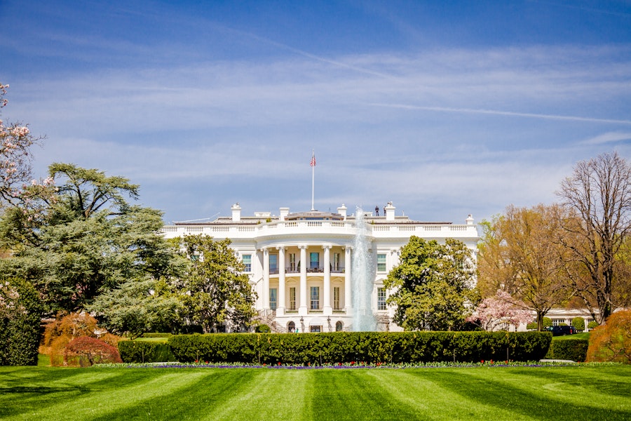 The White House with a green lawn, running fountains and trimmed bushes in front. 