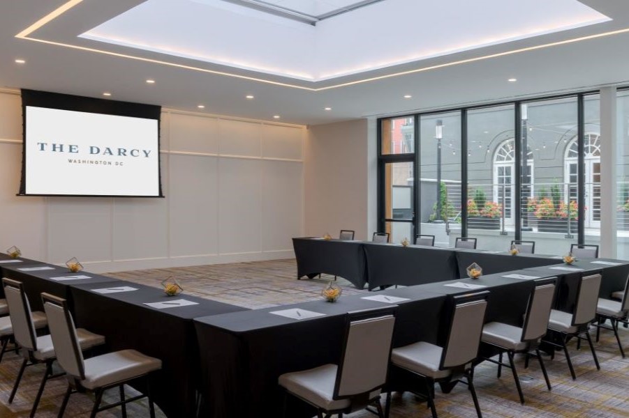 A modern, well-lit conference room at The Darcy in Washington, DC, featuring a U-shaped table setup with comfortable chairs and large windows letting in natural light.