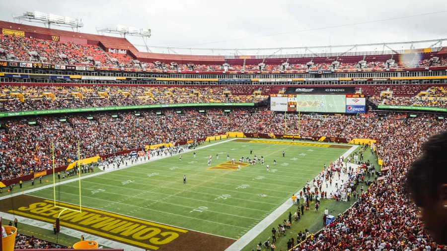 A packed stadium during a Washington Commanders football game, with fans filling the stands and players on the field at FedExField.