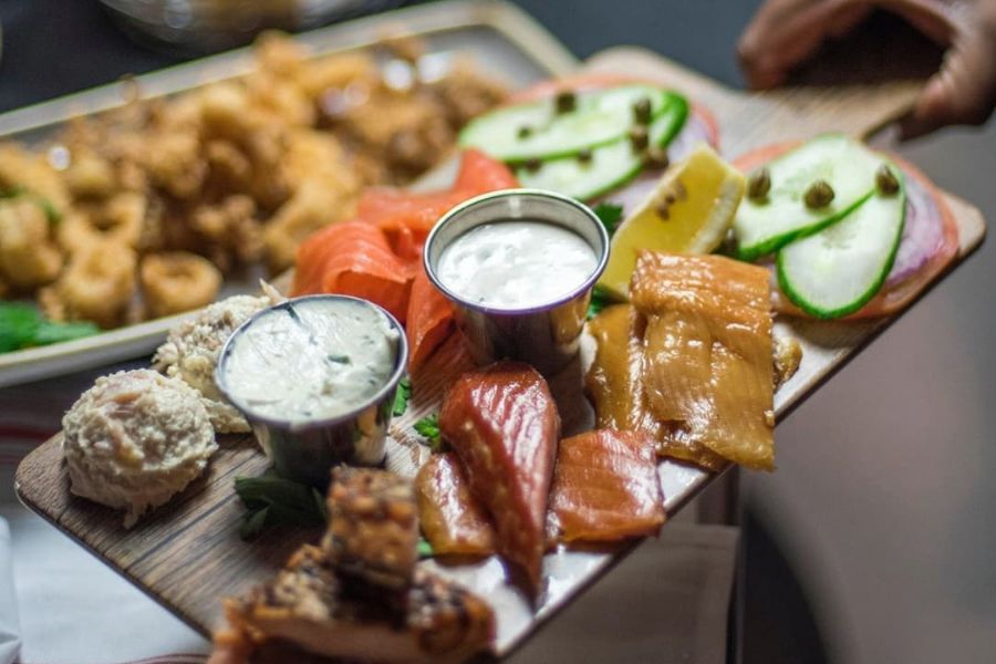 Smokehouse Fish Board from Ivy City Smokehouse featuring two white dips, an array of fish and cucumbers