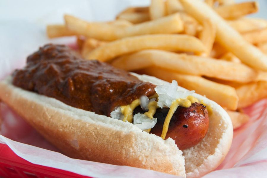 This image shows a chili half-smoke from Ben's Chili Bowl, a DC classic featuring a grilled sausage topped with chili, mustard, and onions, served with fries.