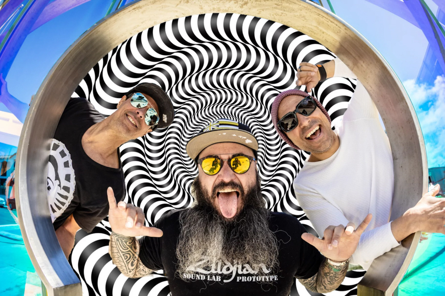 Band Pepper poses playfully in front of a hypnotic black-and-white spiral backdrop, with bright sunglasses, casual