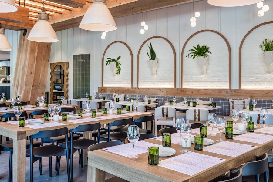 A bright, airy dining space with wooden tables, greenery, and elegant lighting, offering a stylish and inviting ambiance.