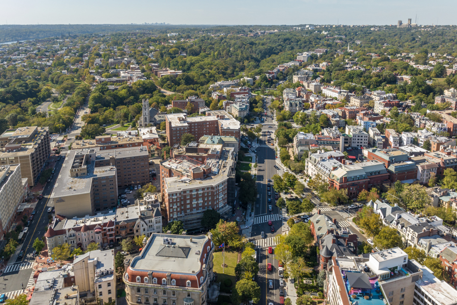 Aerial view of a tree-lined neighborhood with historic and modern buildings along Massachusetts Avenue.