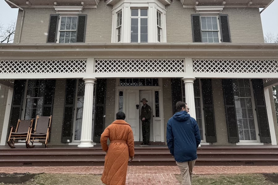 Visitors approach the front steps of a historic house on a snowy day, where a park ranger waits at the entrance.