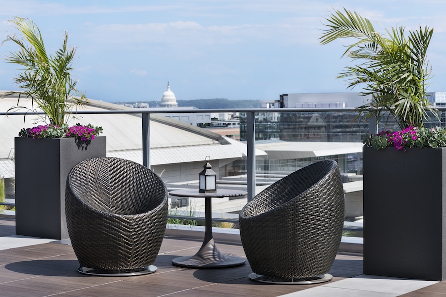 A stylish rooftop lounge with woven chairs, potted plants and a view of the US Capitol in Washington, DC.