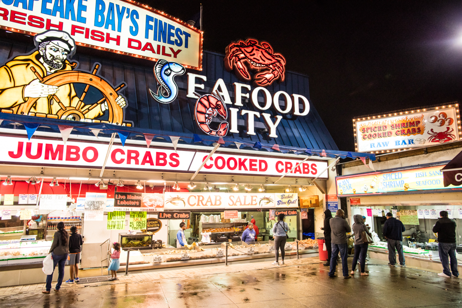 Visitors browse fresh seafood stalls at the historic Municipal Fish Market in D.C., illuminated by neon signs at night.